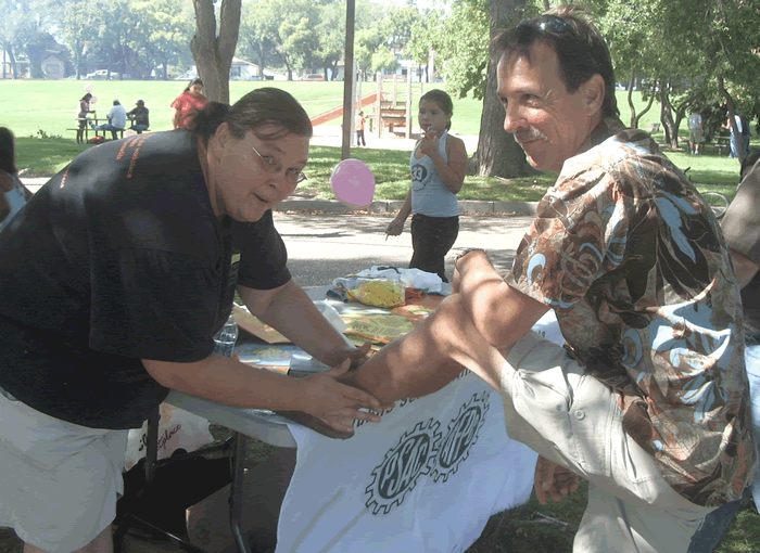 Photo of Marianne Hladun applying a tattoo to the leg of Larry Hubich, President of the Saskatchewan Federation of Labour