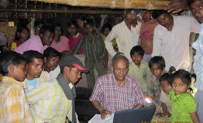Photo of Harmesh showing villagers the benefits of newly-installed solar-power for lighting and computers